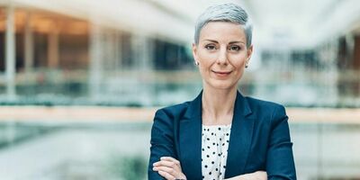 En dame med blazer står med armene foldet. Foto