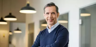En mann står med armene i kors og smiler. Foto