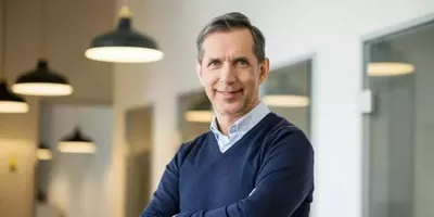 En mann står med armene i kors og smiler. Foto