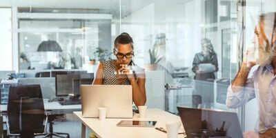 To mennesker sitter inne på et kontor og jobber. Foto